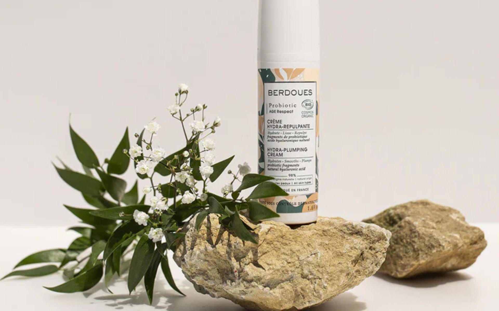 Crème hydra-repulpante Berdoues mise en scène avec des fleurs blanches sur une pierre, illustrant un soin du corps hydratant.