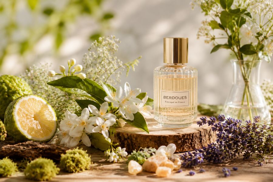 flacon de parfum entouré de fleurs, agrumes et plantes aromatiques évoquant des odeurs naturelles en parfumerie