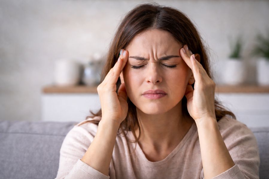 Femme se tenant les tempes avec une expression de douleur, illustrant un mal de tête lié à une sensibilité aux odeurs ou aux parfums.
