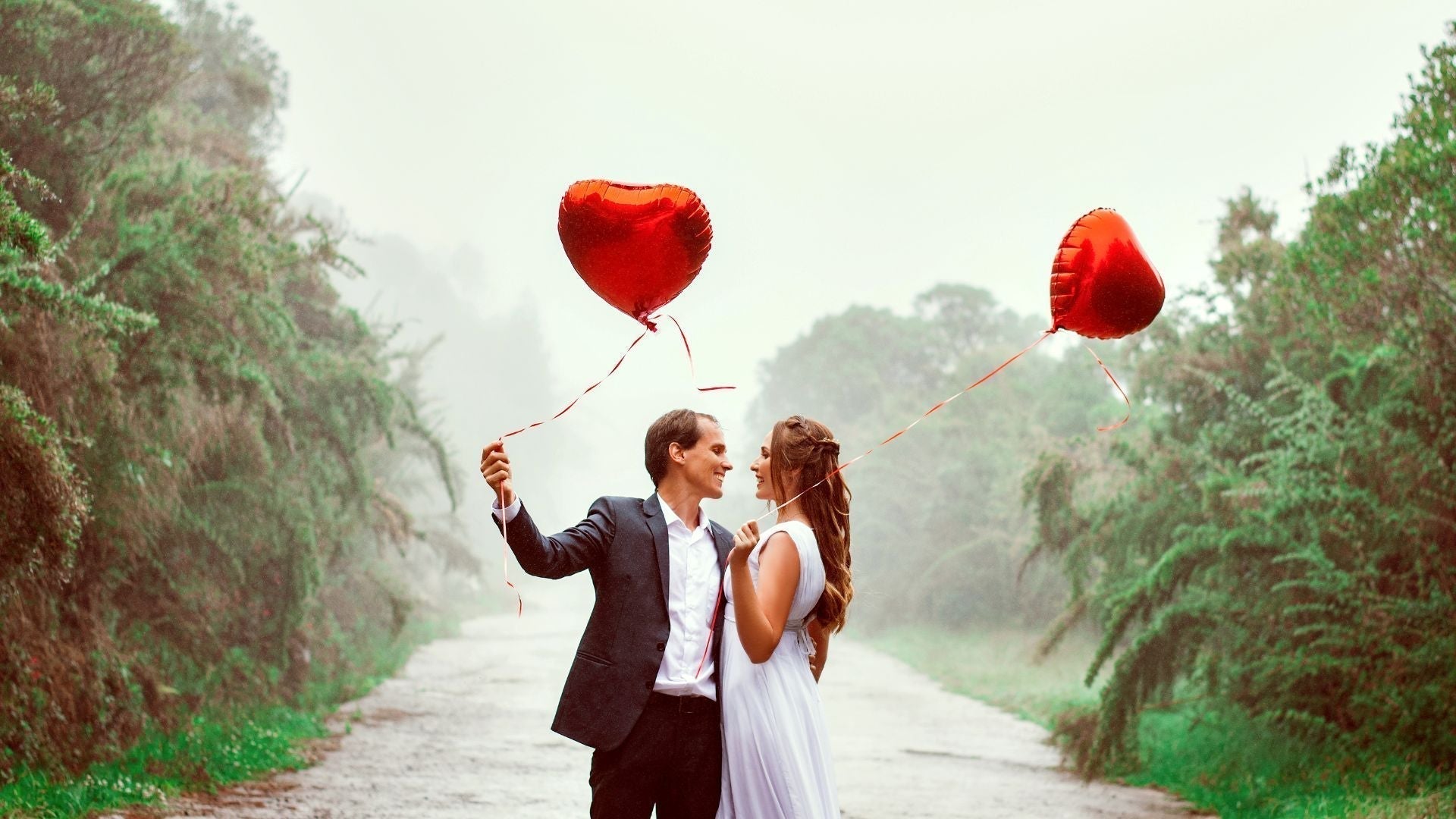 Un couple amoureux tenant des ballons en forme de cœur, symbolisant la Saint-Valentin, dans un décor romantique et naturel.