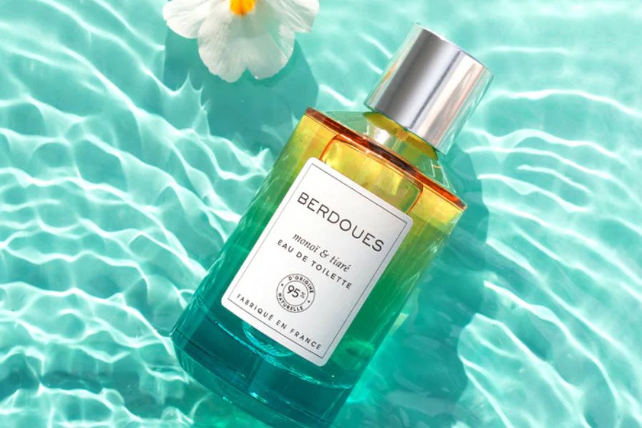 Flacon d’Eau de Toilette Monoï & Tiaré Berdoues posé sur une eau turquoise avec une fleur blanche, symbole de fraîcheur estivale.